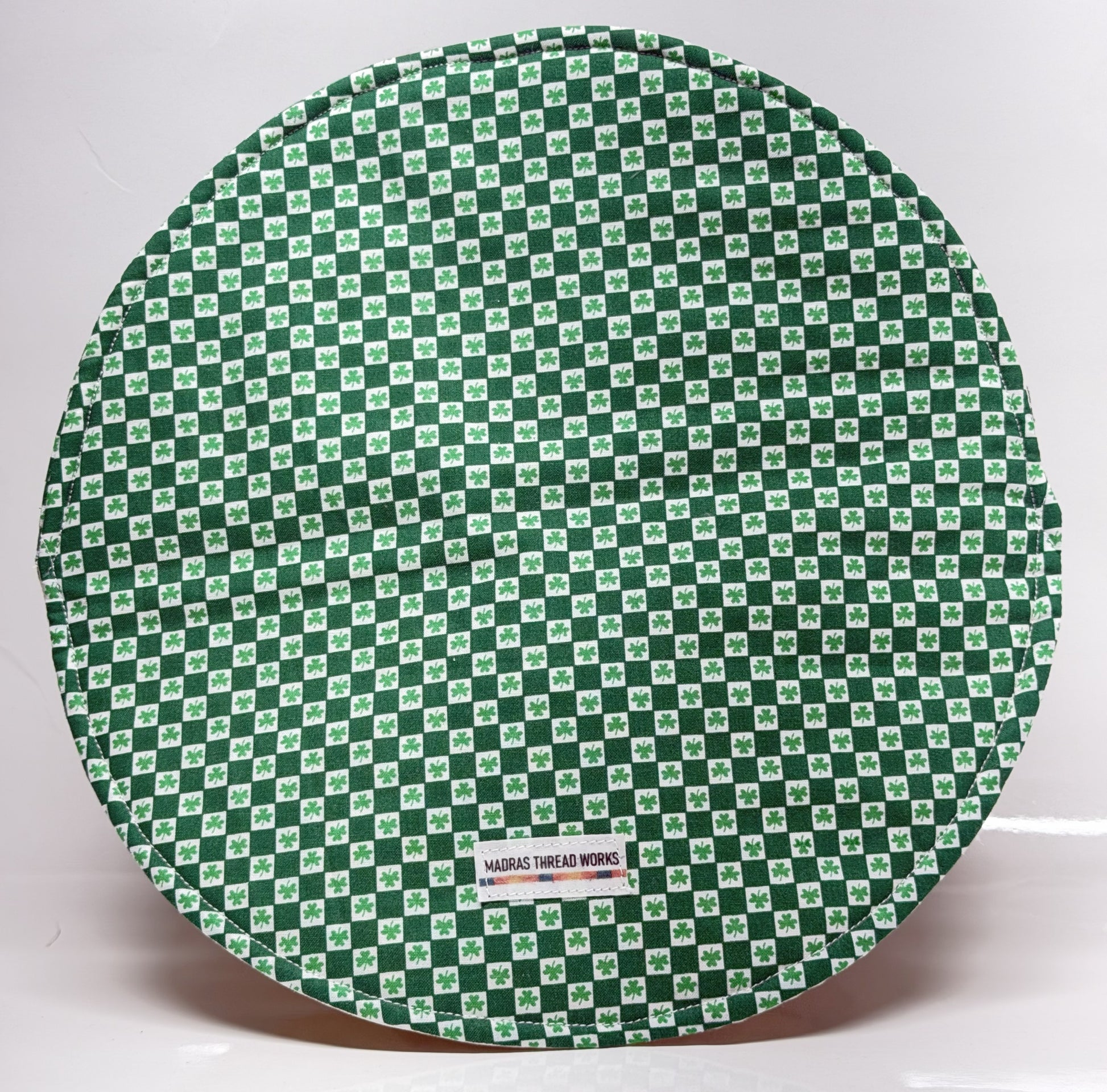 Round green and white checkered mat with a visible brand label on a white background
